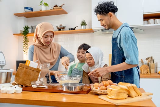 Front view of muslim mother show example to mix flour in the bowl for her child to make the bakery in kitchen of their house.
