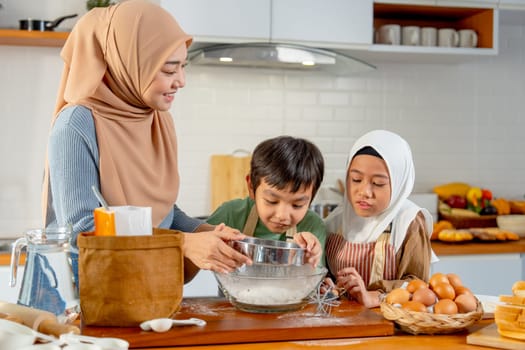 Little boy and girl of muslim family help and learn from their mother to cook relate to cooking flour and ingredients in the kitchen with happiness.