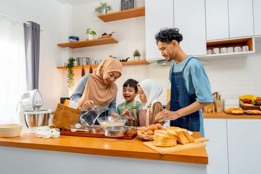 Muslim mother pour the water in jar to mixed flour in the bowl for teach her child to make the bakery in kitchen of their house.