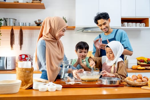 Asian muslim father, mother and brother cheer up the girl to mix flour in the bowl and stay together in kitchen of their house.