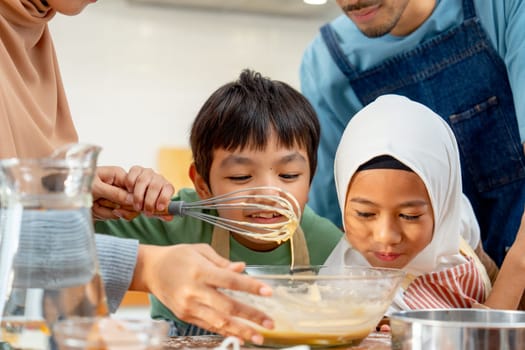 Little Asian boy and girl show smell action after mix flour in the bowl and enjoy with family in the kitchen of their house.