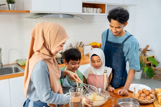 Muslim mother show example to mix flour in the bowl for her child to make the bakery in kitchen of their house.