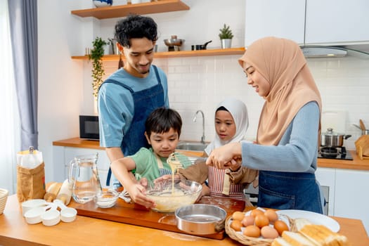 Muslim family with father, mother, boy and girl enjoy to make the bakery with mix flour in bowl and stay together in kitchen with happiness.