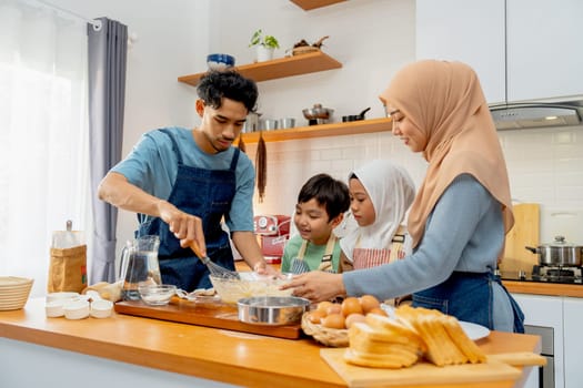 Young Asian father mix flour in the bowl during make the bakery together with his muslim family with wife and child in the kitchen of their house.