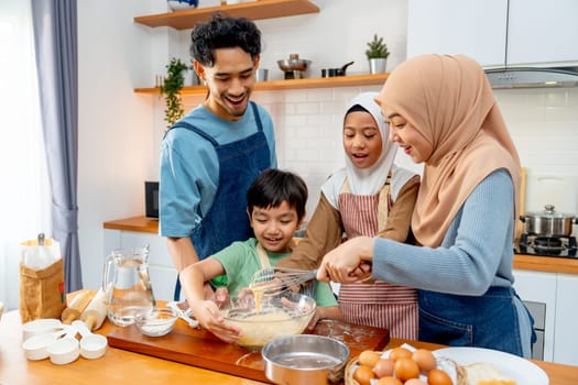 Wide shot of muslim family with father, mother, boy and girl enjoy to make the bakery with mix flour in bowl and stay together in kitchen with happiness.