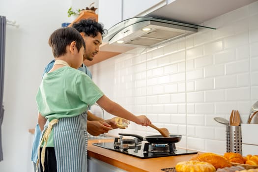 Back of young Asian father show skill of cooking by throwing pan cake up and his son cheer up beside in the kitchen of their house.
