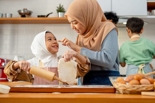 Young Asian muslim mother and daughter tease and enjoy to make some bakery together in the kitchen.