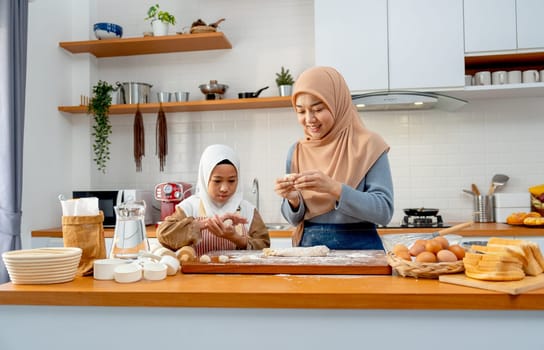 Wide shot of Asian muslim mother teach her daughter to threshing flour to be like ball shape for making bakery together in kitchen of their house.