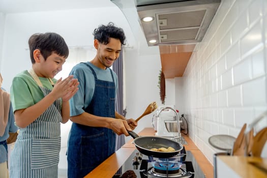 Young Asian father enjoy to teaching to make pan cake for his son who cheer up beside in the kitchen of their house.