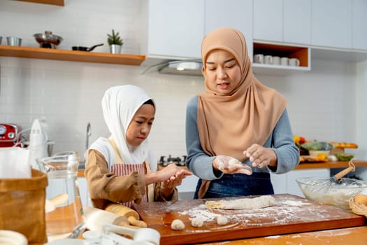 Asian muslim mother teach her daughter to threshing flour to be like ball shape for making bakery together in kitchen of their house.