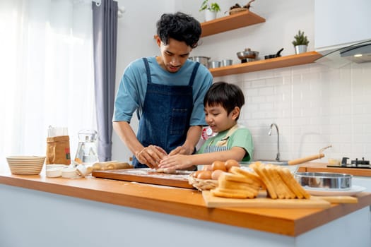 Wide shot of Asian father stand beside his son during teaching the boy to threshing flour for making bakery in kitchen of their house.