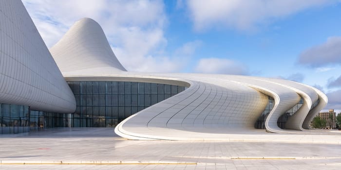 Heydar Aliyev Centre in Baku, Azerbaijan, exemplifies contemporary architecture with its fluid, wave-inspired design against a backdrop of cloudy blue sky. Designed by renowned architect Zaha Hadid