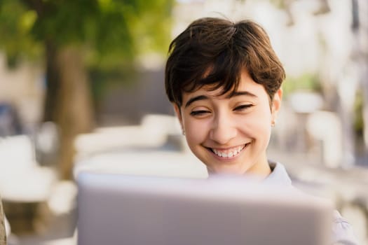 A bright young individual radiates joy using a sleek laptop outdoors, embodying remote work, creativity, and productivity in a serene setting that encourages focus and inspiration
