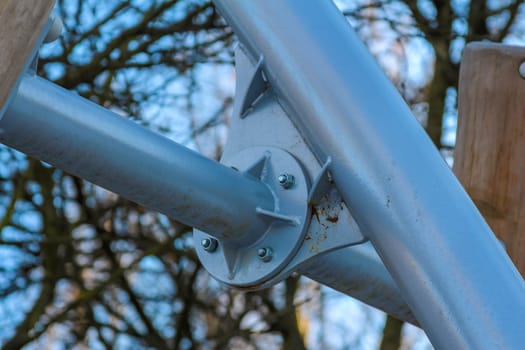 Close-up view of a playground metal support, showcasing its design and structure against a bright sky and tree branches.