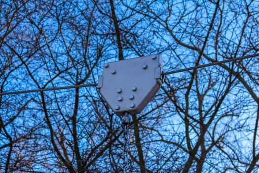 A metal pulley is suspended from a cable, framed by the intricate branches of leafless trees under a bright blue winter sky.