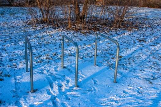 Metal exercise bars stand on a snowy ground in a park, surrounded by trees, inviting fitness activities in winter.