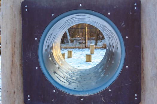 Children can enjoy outdoor playtime in a snowy park featuring a large slide opening, surrounded by wooden posts and trees.
