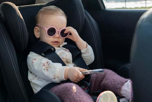 A baby with pink sunglasses, comfortably seated in a car seat, showing off a playful and stylish look. Concept of safety, travel, and fashionable childhood moments