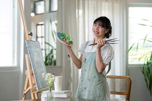 Portrait of a young female artist working on an abstract acrylic canvas painting in an art painting studio..