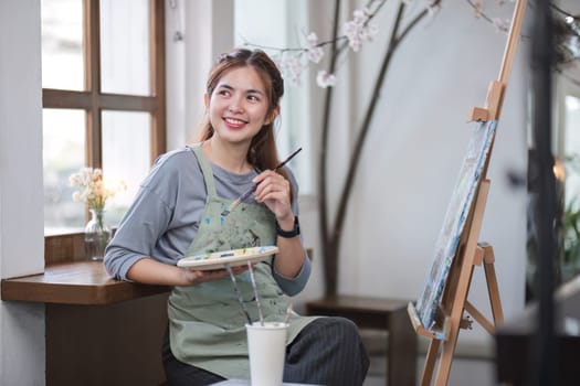 Portrait of a young female artist working on an abstract acrylic canvas painting in an art painting studio..