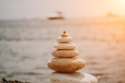 Pyramid stones on the seashore with warm sunset on the sea background. Happy holidays. Pebble beach, calm sea, travel destination. Concept of happy vacation on the sea, meditation, spa, calmness.