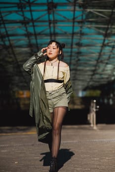 A beautiful Asian woman in shorts and a green leather coat comes out of the subway