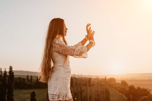 Romantic beautiful bride in white dress posing with sea and mountains in background. Stylish bride standing back on beautiful landscape of sea and mountains on sunset