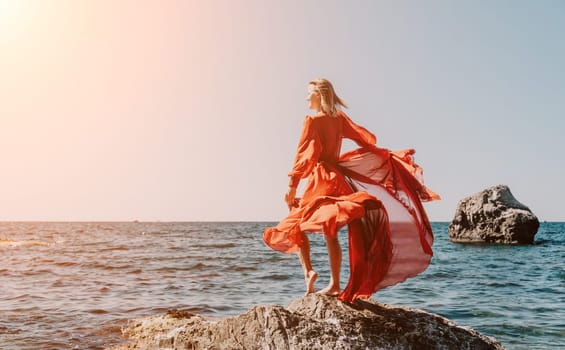 Woman travel sea. Young Happy woman in a long red dress posing on a beach near the sea on background of volcanic rocks, like in Iceland, sharing travel adventure journey