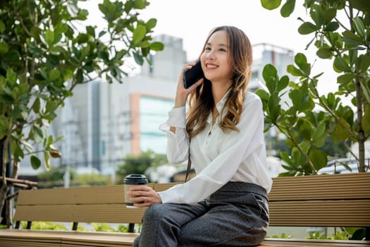 Asian business young woman using mobile smartphone talking on cellphone outdoor corporate building exterior, Happy smiling businesswoman sitting talk on mobile phone outside street city near office