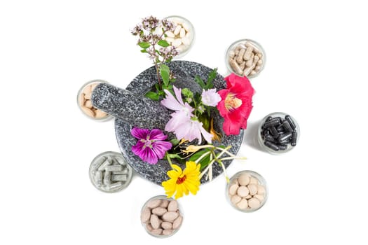 Capsules on green leaf of sage, brown jar, wooden mortar with a sprig of mint, flowers of chamomile, clover, oregano, mignonette, elecampane isolated on white background