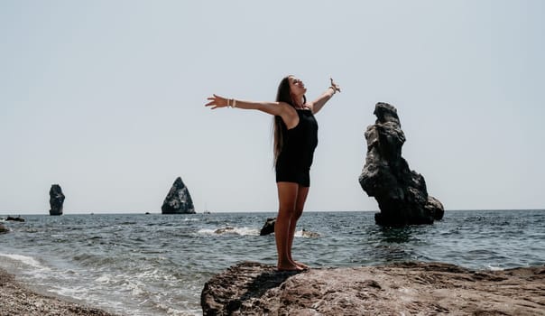 Woman travel sea. Young Happy woman in a long red dress posing on a beach near the sea on background of volcanic rocks, like in Iceland, sharing travel adventure journey