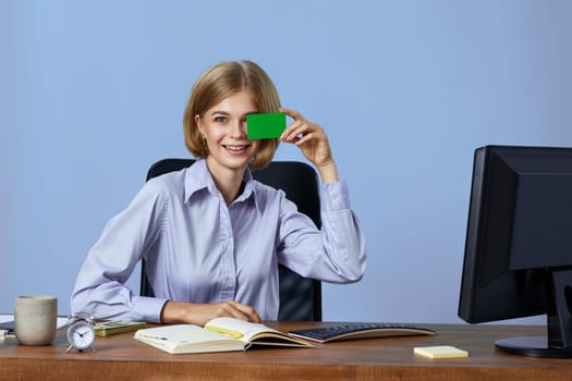 cheerful blonde female business manager holding plastic credit card on blue background