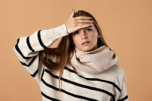 Young woman in wool sweater suffering from headache on beige background. pain and migraine