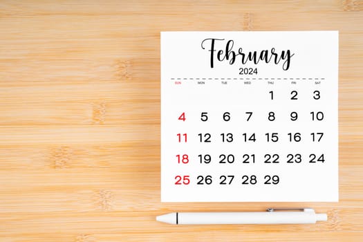 February 2024 calendar page and pen on wooden background with empty space.