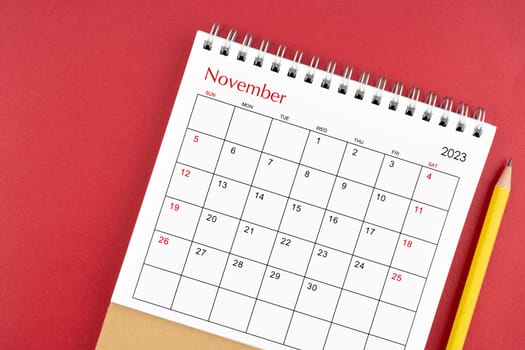 November 2023 desk calendar and pencil on red color background.