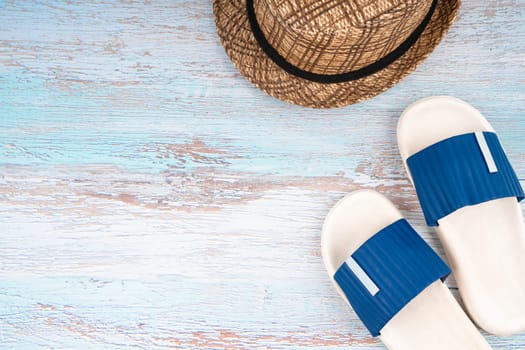 Blue sandals and straw hat with copy-space on blue wooden background.