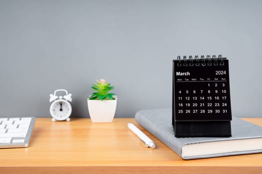 March 2024 black color desk calendar on wooden table with diary.