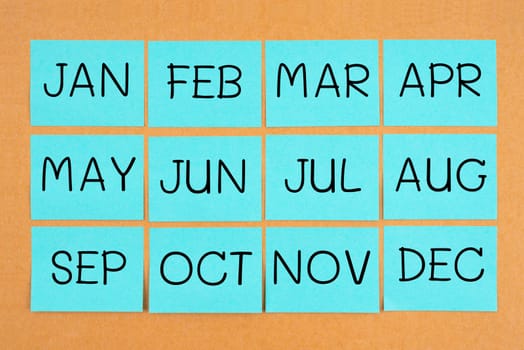 12 months acronyms on blue sticky notes calendar. On wooden board.
