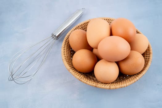 chicken eggs with egg whisk on blue wooden background. 