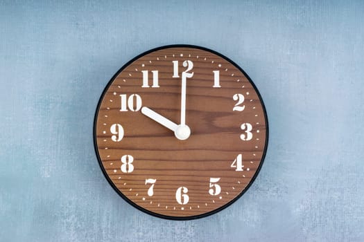 Brown Wooden clock placed in middle of blue cement wall.