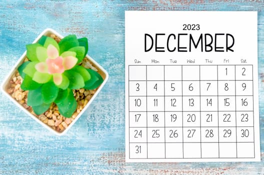 December 2023 Monthly calendar with plant pot on wooden background.