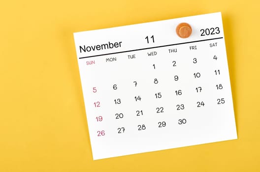 November 2023 and wooden push pin on yellow background.