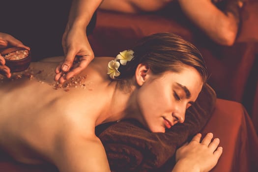 Couple customer having exfoliation treatment in luxury spa salon with warmth candle light ambient. Salt scrub beauty treatment in Health spa body scrub. Quiescent