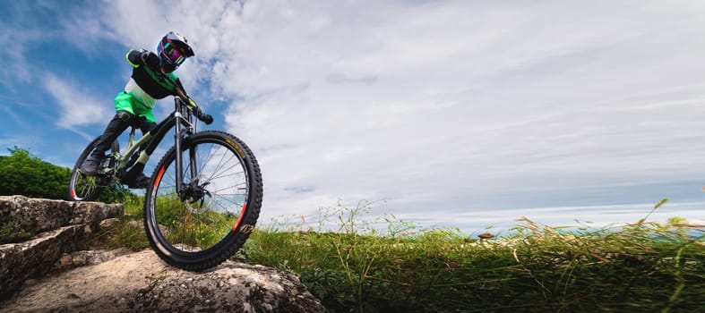 Sport. A guy in protective clothing on a mountain bike on a rock. A man in a bright green T-shirt quickly descends the mountain. Extreme sport.