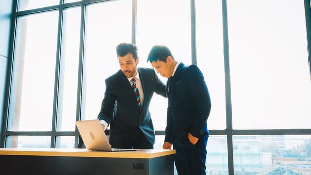 Two business people talk project strategy at office meeting room. Businessman discuss project planning with colleague at modern workplace while having conversation and advice on financial report. Jivy