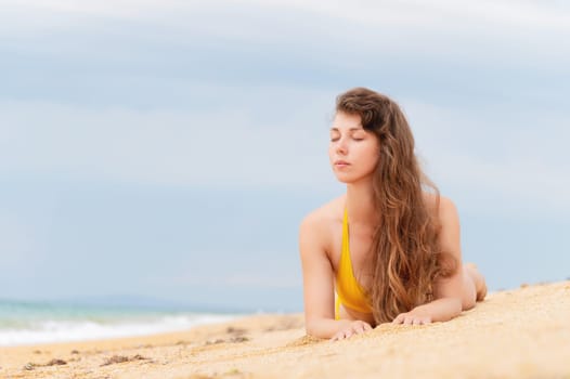 Beautiful woman with perfect body lies on sandy beach, wearing yellow bikini, sunbathing at beach resort, enjoying summer vacation.