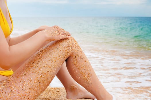 A close-up shot of wet sand clinging to the feet of a girl sitting on the sea in a swimsuit, in daylight. Sandy feet of an unrecognizable woman on the beach