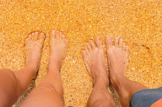 Top view from a couple standing on the sand, romantic. Love story. Female and male legs stand side by side on the sandy beach first person view.