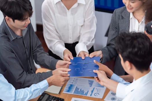 Corporate officer worker collaborate in office, connecting puzzle pieces with report paper on table as partnership and teamwork. Unity and synergy in business concept by merging jigsaw puzzle. Concord