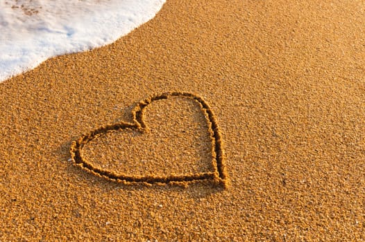 Heart drawn on the beach. hand written love sign on the sand with a wave in the background.